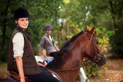 A young couple horseback riding in the forest.